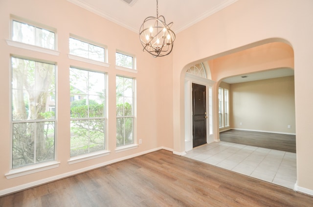 spare room with plenty of natural light, ornamental molding, a chandelier, and light hardwood / wood-style flooring