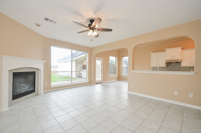 unfurnished living room with ceiling fan, a healthy amount of sunlight, light tile patterned floors, and a tiled fireplace