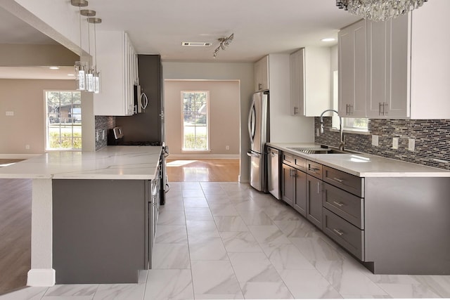 kitchen with white cabinets, sink, hanging light fixtures, appliances with stainless steel finishes, and kitchen peninsula