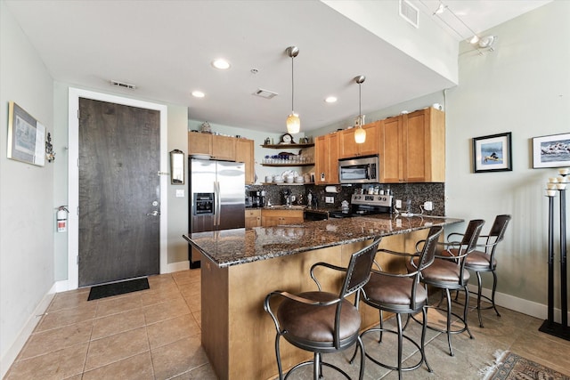 kitchen with decorative backsplash, appliances with stainless steel finishes, dark stone counters, light tile patterned floors, and hanging light fixtures