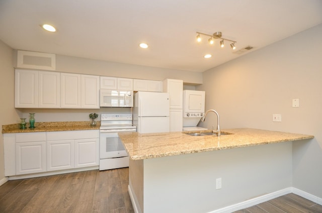 kitchen with white appliances, white cabinets, sink, stacked washer and dryer, and dark hardwood / wood-style flooring