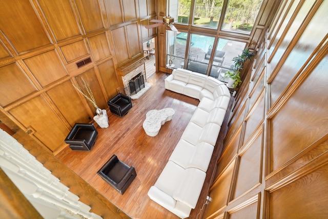 living room featuring hardwood / wood-style floors, wooden walls, ceiling fan, a towering ceiling, and a fireplace