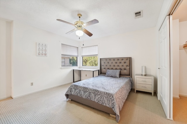 bedroom featuring ceiling fan, light colored carpet, a textured ceiling, and a closet