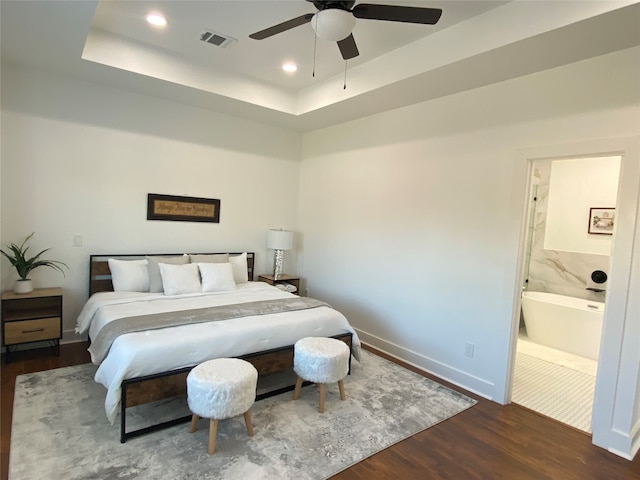 bedroom featuring a raised ceiling, ceiling fan, ensuite bathroom, and dark hardwood / wood-style floors