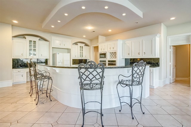 kitchen with white refrigerator with ice dispenser, decorative backsplash, white cabinetry, and a kitchen island with sink