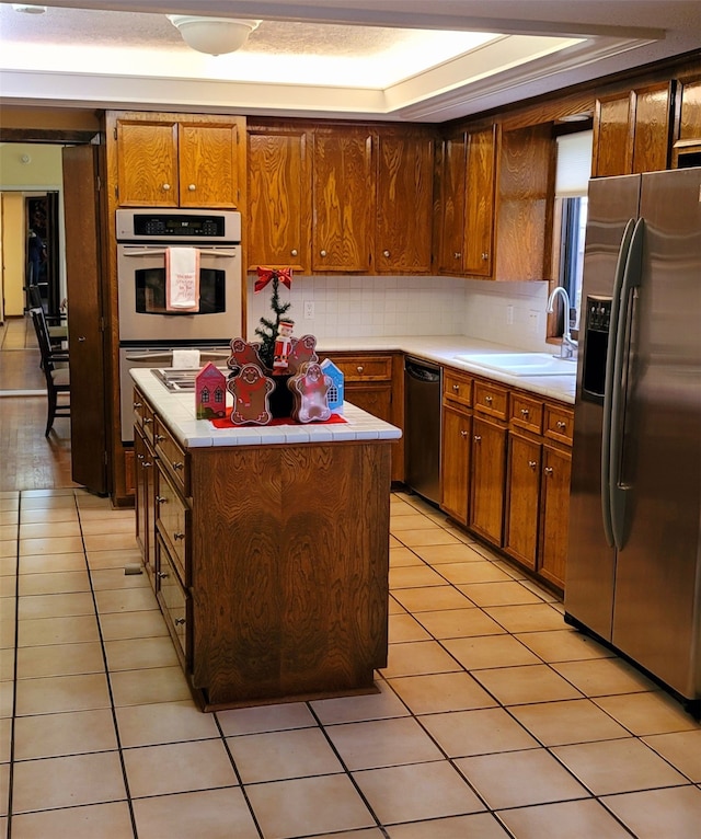 kitchen with stainless steel appliances, a tray ceiling, sink, a kitchen island, and light tile patterned flooring