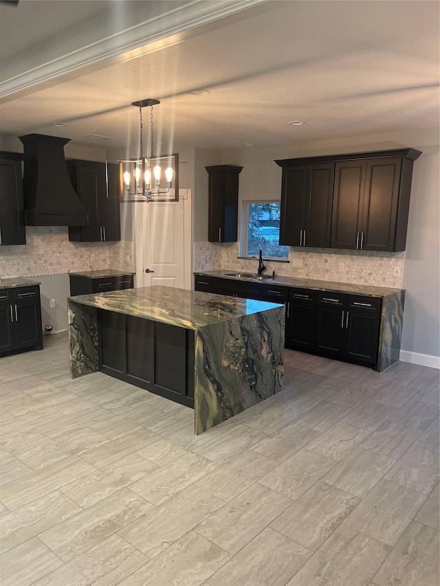 kitchen featuring decorative backsplash, hanging light fixtures, custom range hood, and dark stone counters