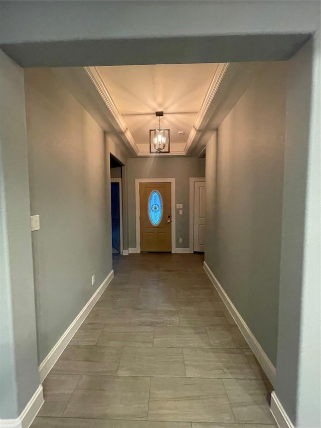 hallway with a chandelier, a raised ceiling, and crown molding