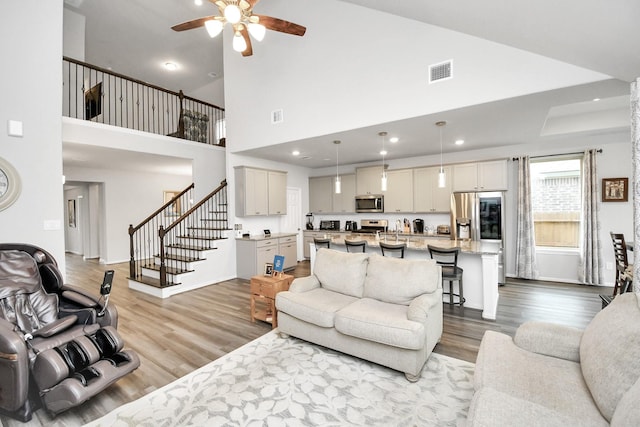 living room featuring ceiling fan, light hardwood / wood-style floors, and a high ceiling