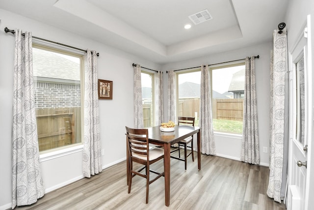 dining area with a tray ceiling, a fireplace, and light hardwood / wood-style flooring