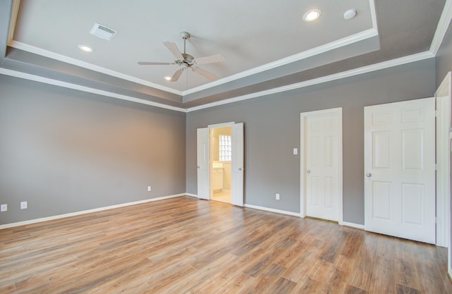 unfurnished bedroom with ornamental molding, a tray ceiling, ceiling fan, light hardwood / wood-style flooring, and connected bathroom