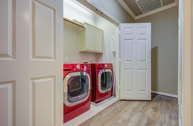 laundry area featuring cabinets, light hardwood / wood-style floors, ornamental molding, and washing machine and clothes dryer