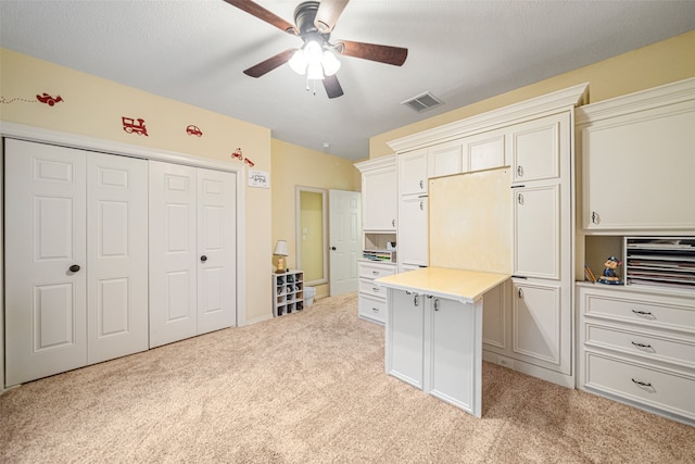 kitchen featuring a textured ceiling, ceiling fan, white cabinets, and light carpet