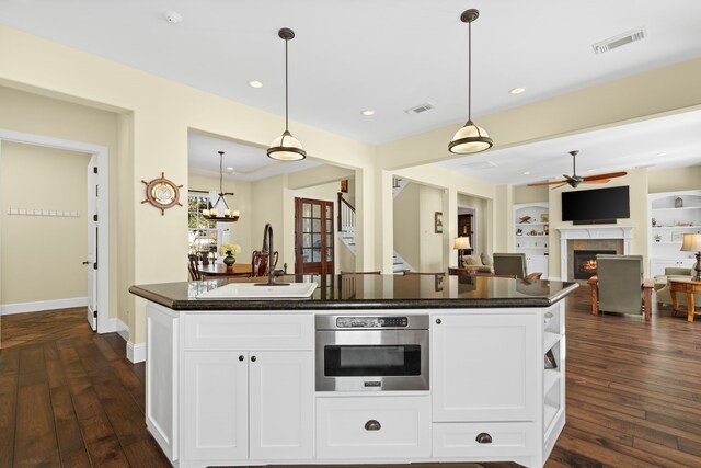 kitchen featuring stainless steel oven, hanging light fixtures, dark wood-type flooring, a center island with sink, and white cabinets