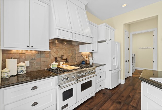 kitchen with dark hardwood / wood-style flooring, premium range hood, white appliances, dark stone countertops, and white cabinets