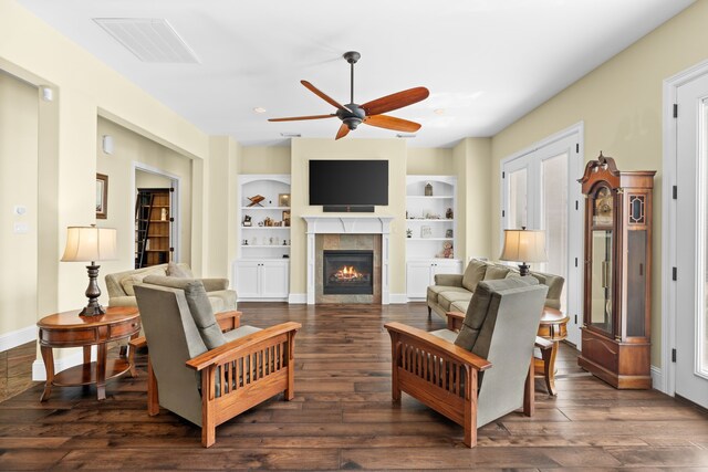 living room featuring a tile fireplace, dark hardwood / wood-style floors, built in features, and ceiling fan