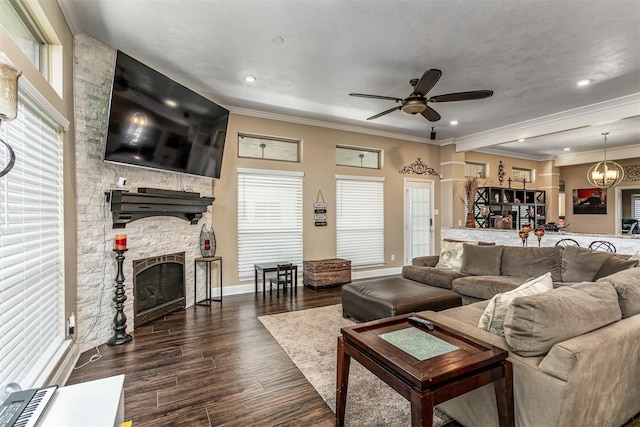 living room with a fireplace, ornamental molding, dark wood-type flooring, and ceiling fan with notable chandelier