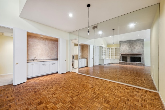 unfurnished living room featuring a stone fireplace, sink, a towering ceiling, and parquet flooring