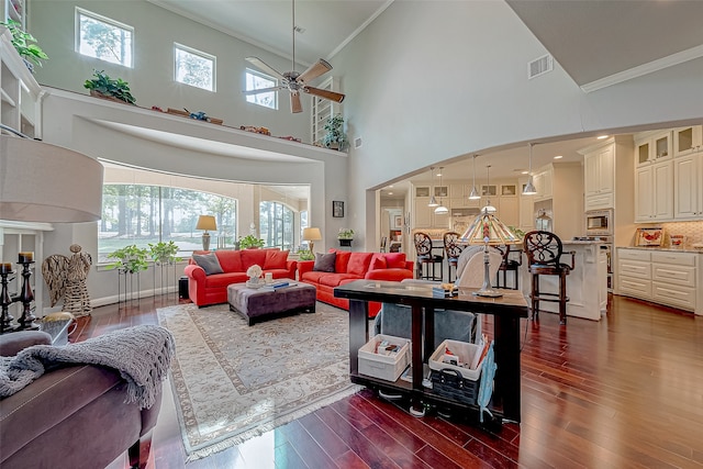 living room with ceiling fan, dark hardwood / wood-style flooring, a towering ceiling, and crown molding