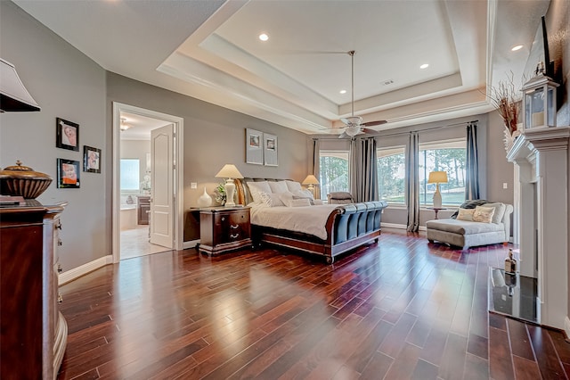 bedroom featuring dark hardwood / wood-style flooring, a tray ceiling, ensuite bath, and ceiling fan