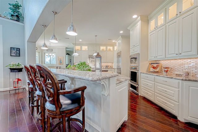 kitchen featuring decorative backsplash, dark hardwood / wood-style flooring, stainless steel appliances, a center island with sink, and white cabinets