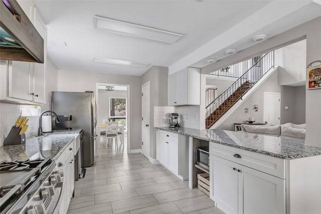 kitchen featuring white cabinets, decorative backsplash, light stone countertops, range hood, and appliances with stainless steel finishes