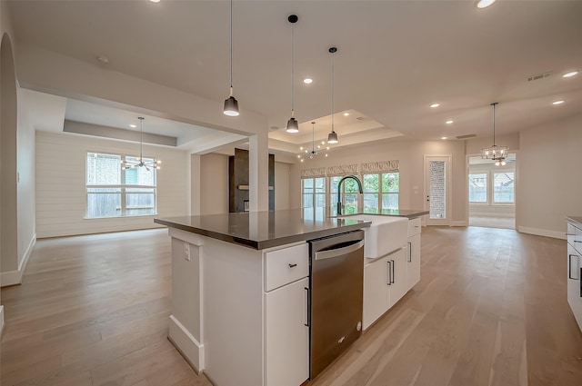 kitchen with an inviting chandelier, a center island with sink, a raised ceiling, stainless steel dishwasher, and white cabinetry