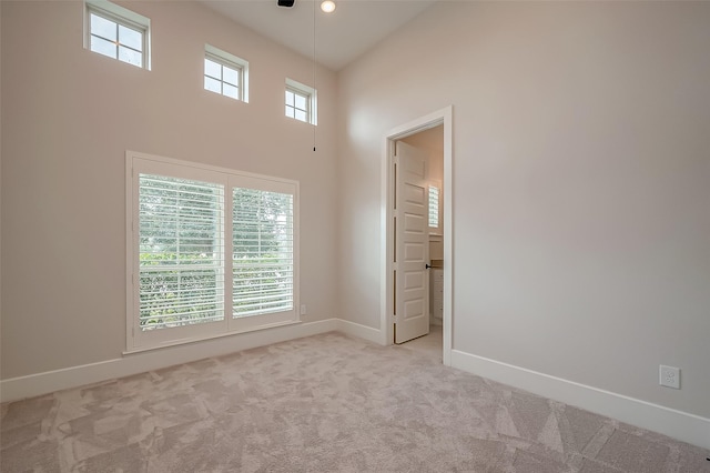 empty room with ceiling fan, a towering ceiling, and light carpet