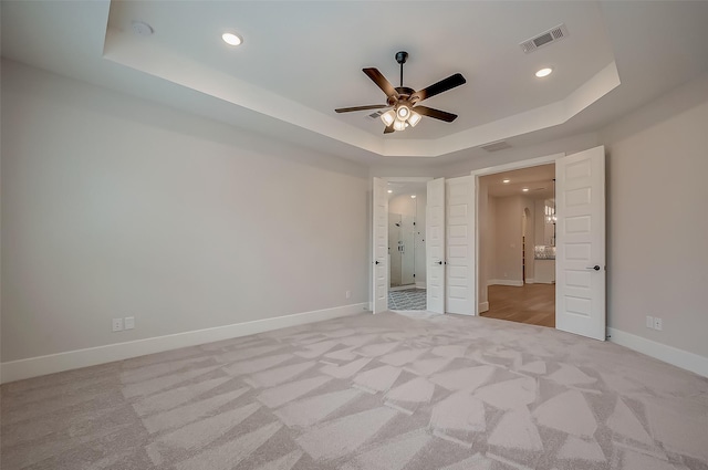 unfurnished bedroom featuring ceiling fan, a raised ceiling, and light colored carpet