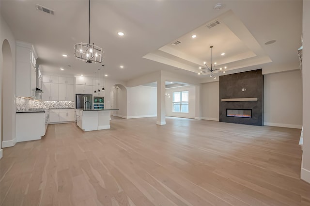 unfurnished living room with light hardwood / wood-style flooring, sink, a fireplace, and a tray ceiling