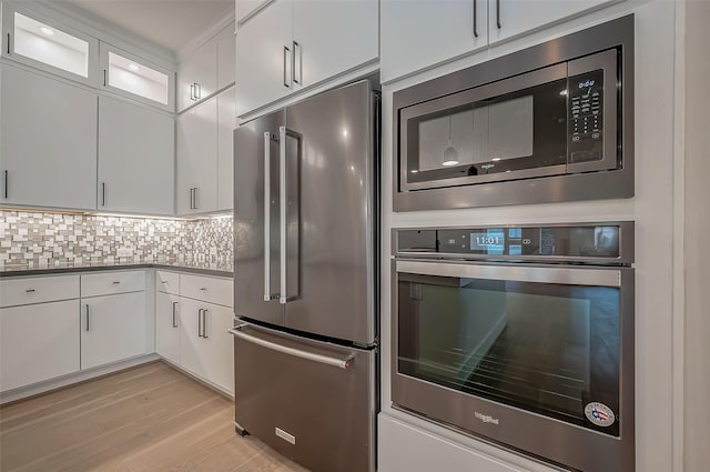 kitchen featuring white cabinets, light hardwood / wood-style flooring, appliances with stainless steel finishes, and tasteful backsplash