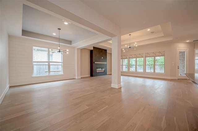 unfurnished living room featuring light hardwood / wood-style floors, a raised ceiling, and an inviting chandelier