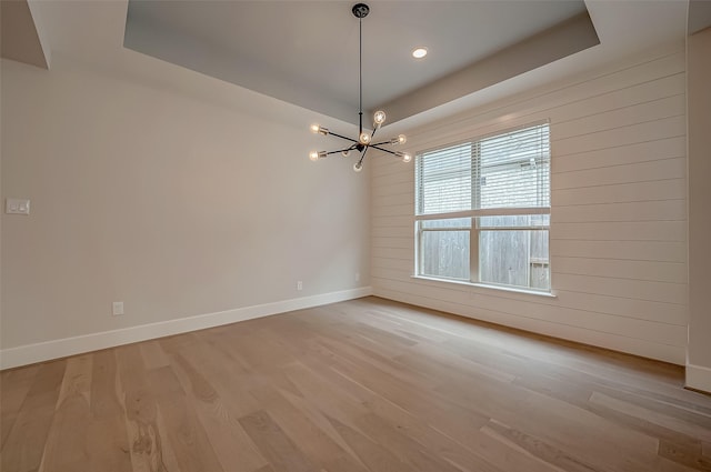 empty room featuring a raised ceiling, a chandelier, light hardwood / wood-style floors, and wood walls