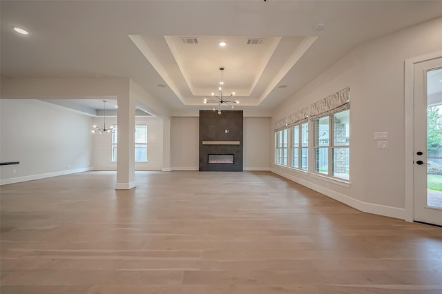 unfurnished living room featuring a chandelier, a large fireplace, light hardwood / wood-style flooring, and a tray ceiling