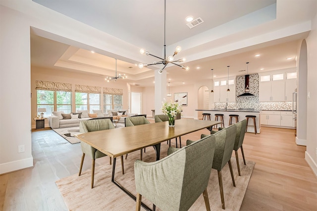 dining space featuring a tray ceiling, sink, light hardwood / wood-style floors, and a notable chandelier