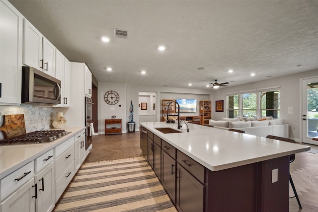 kitchen featuring white cabinets, sink, a textured ceiling, appliances with stainless steel finishes, and an island with sink