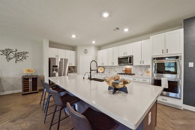 kitchen featuring dark parquet flooring, a spacious island, sink, appliances with stainless steel finishes, and a kitchen bar