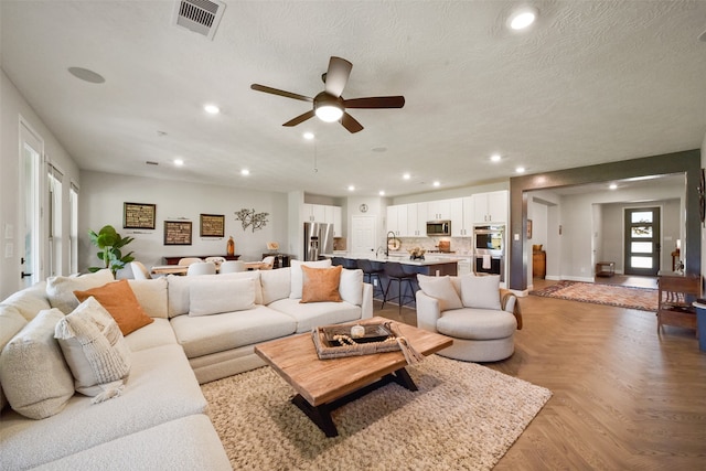 living room with ceiling fan, sink, a textured ceiling, and light parquet flooring