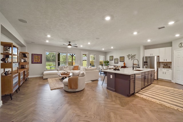 kitchen featuring appliances with stainless steel finishes, ceiling fan, a kitchen island with sink, sink, and white cabinetry