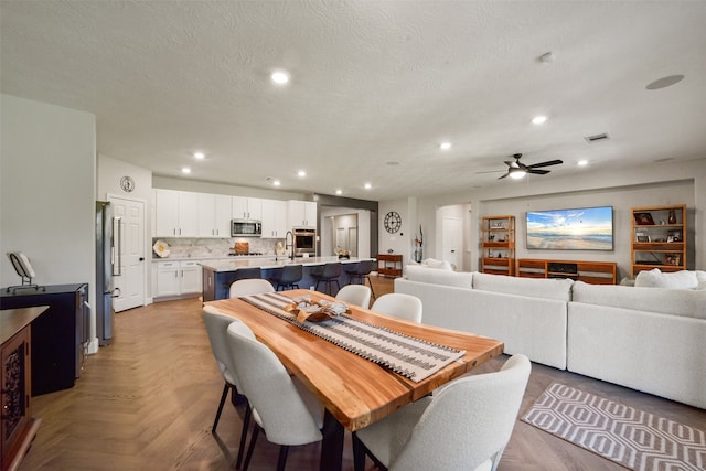 dining space with ceiling fan, light parquet floors, and a textured ceiling