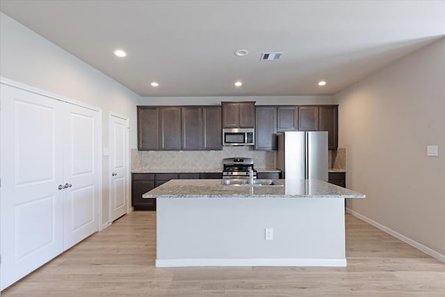 kitchen with sink, light stone counters, stainless steel appliances, and a kitchen island with sink