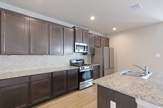 kitchen with backsplash, sink, light hardwood / wood-style flooring, light stone countertops, and stainless steel appliances