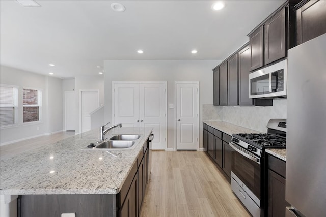 kitchen featuring light stone countertops, appliances with stainless steel finishes, a kitchen island with sink, sink, and light hardwood / wood-style flooring