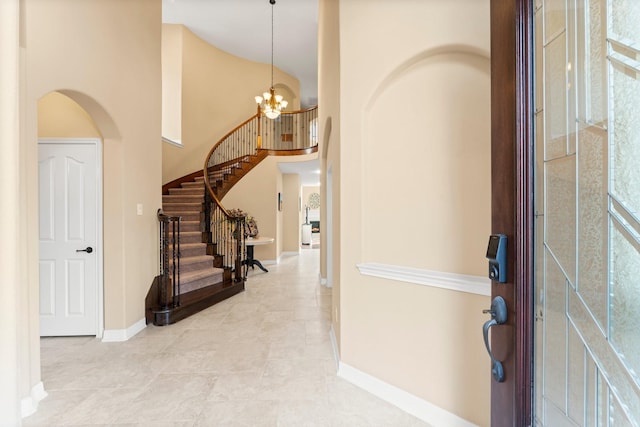 foyer entrance with a notable chandelier, stairway, arched walkways, baseboards, and a towering ceiling