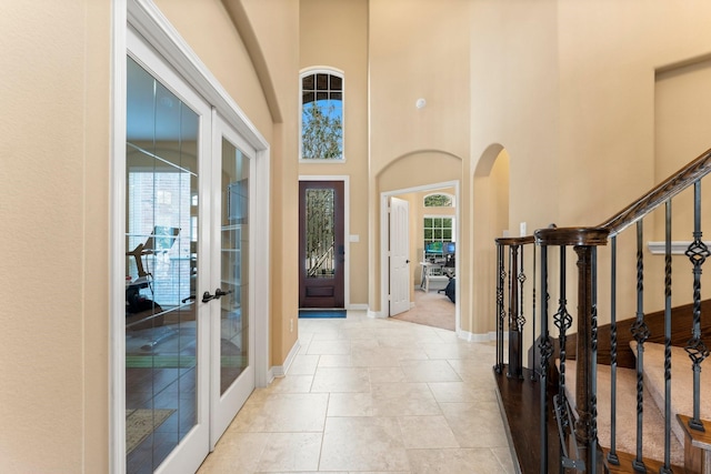 foyer featuring baseboards, stairway, french doors, a towering ceiling, and arched walkways