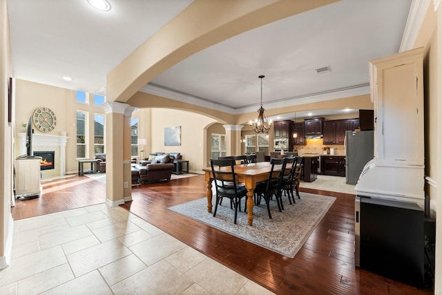 dining space featuring a high end fireplace, ornamental molding, wood finished floors, arched walkways, and a notable chandelier