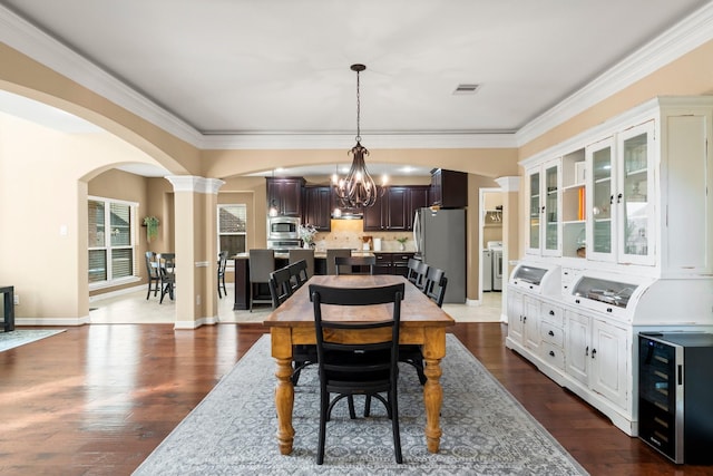 dining area with dark hardwood / wood-style flooring, ornamental molding, washer and clothes dryer, an inviting chandelier, and wine cooler