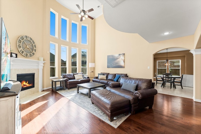 living room with a tiled fireplace, arched walkways, ceiling fan, and wood finished floors