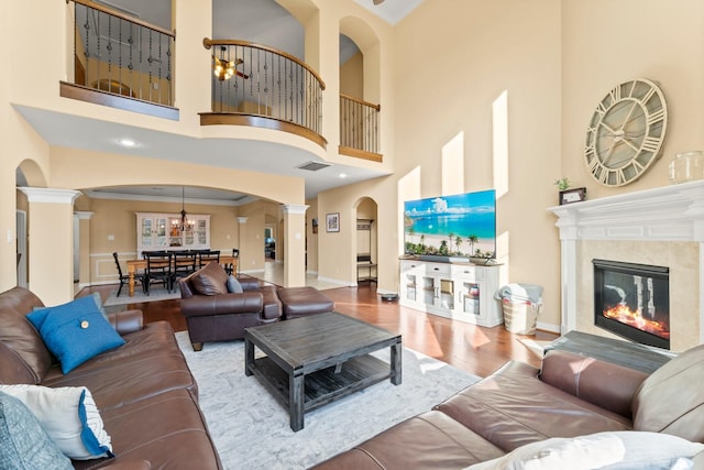 living area featuring visible vents, wood finished floors, a high end fireplace, crown molding, and decorative columns