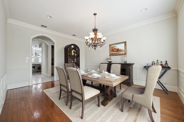 dining space featuring wood-type flooring, ornamental molding, and an inviting chandelier